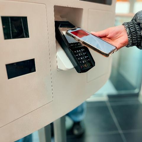 A user tapping a contactless smart phone at kiosk payment terminal.