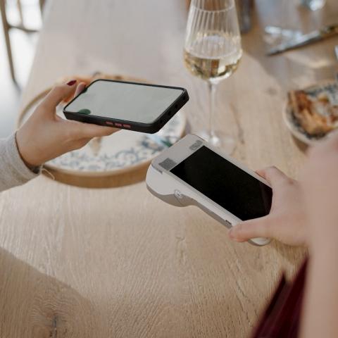 A customer tapping a smart phone with a mobile payment terminal at a restaurant table.