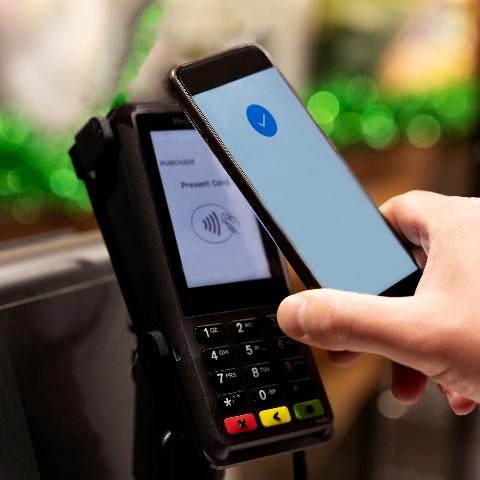 A customer tapping a contactless payment terminal as a cashier desk.